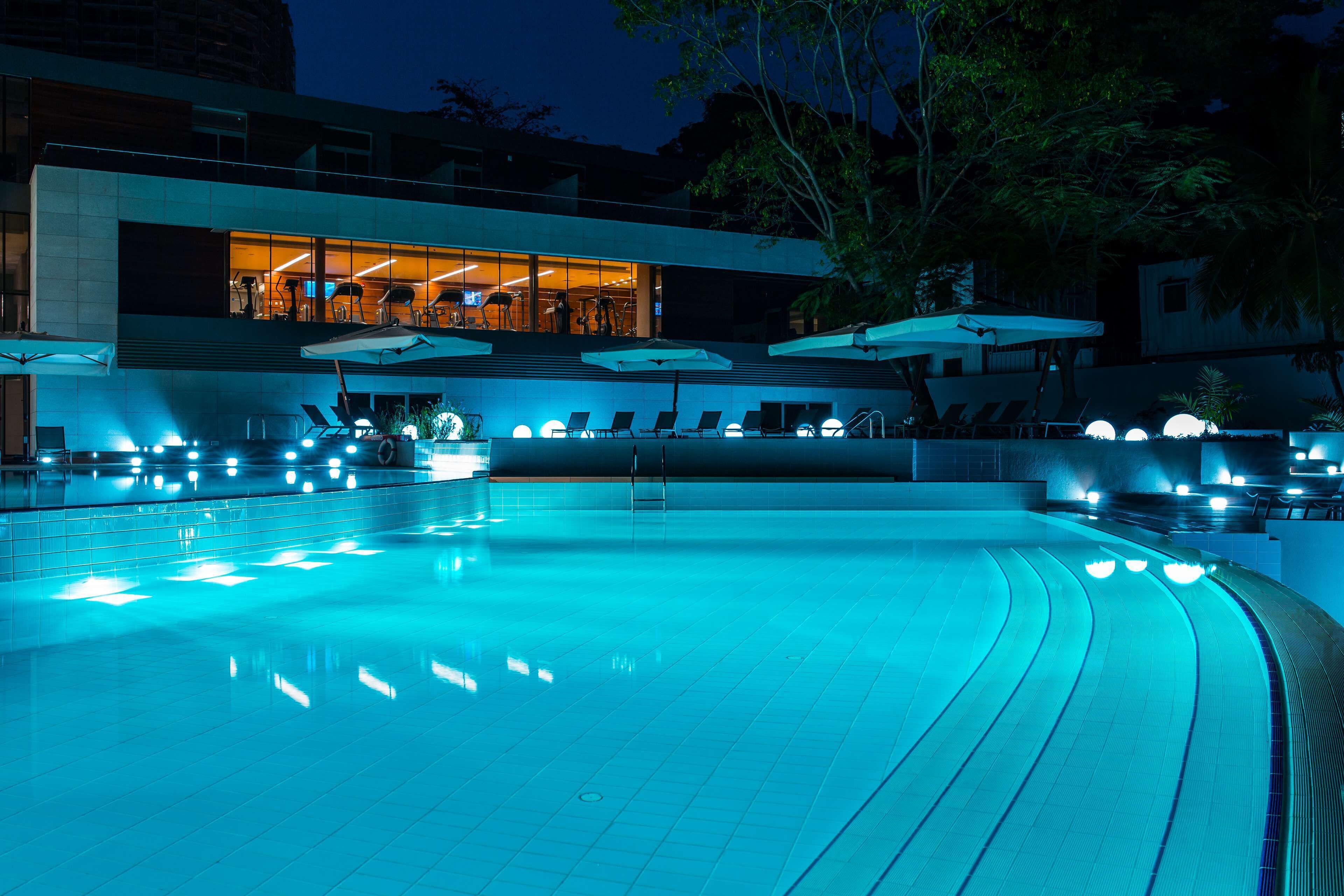 A swimming pool with a modern design, surrounded by lounge chairs and umbrellas, and a building with large windows in the background.
