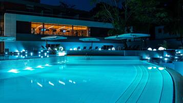 A swimming pool with a modern design, surrounded by lounge chairs and umbrellas, and a building with large windows in the background.