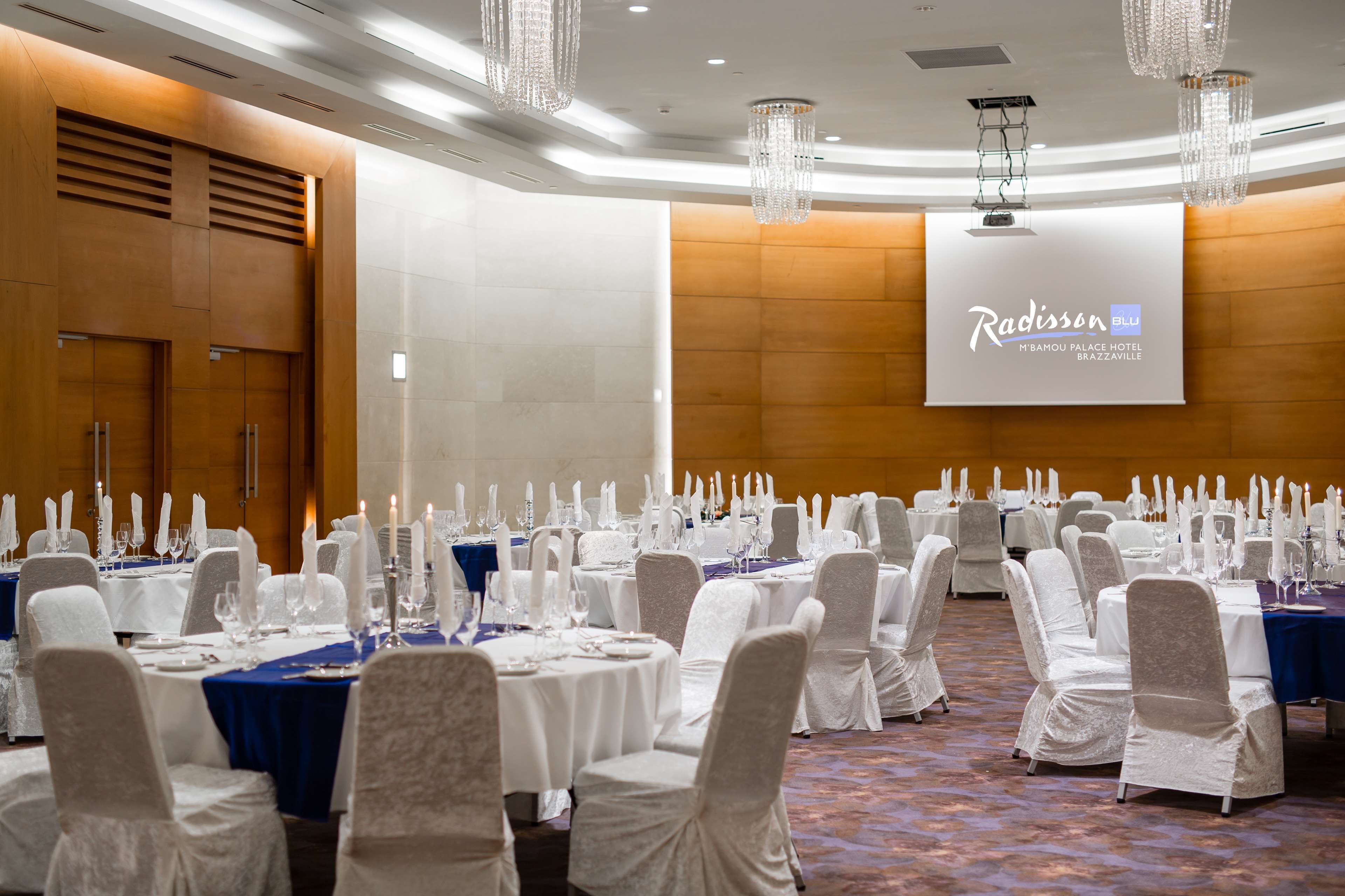 A banquet hall with round tables set for a formal event, featuring white chairs and blue tablecloths.