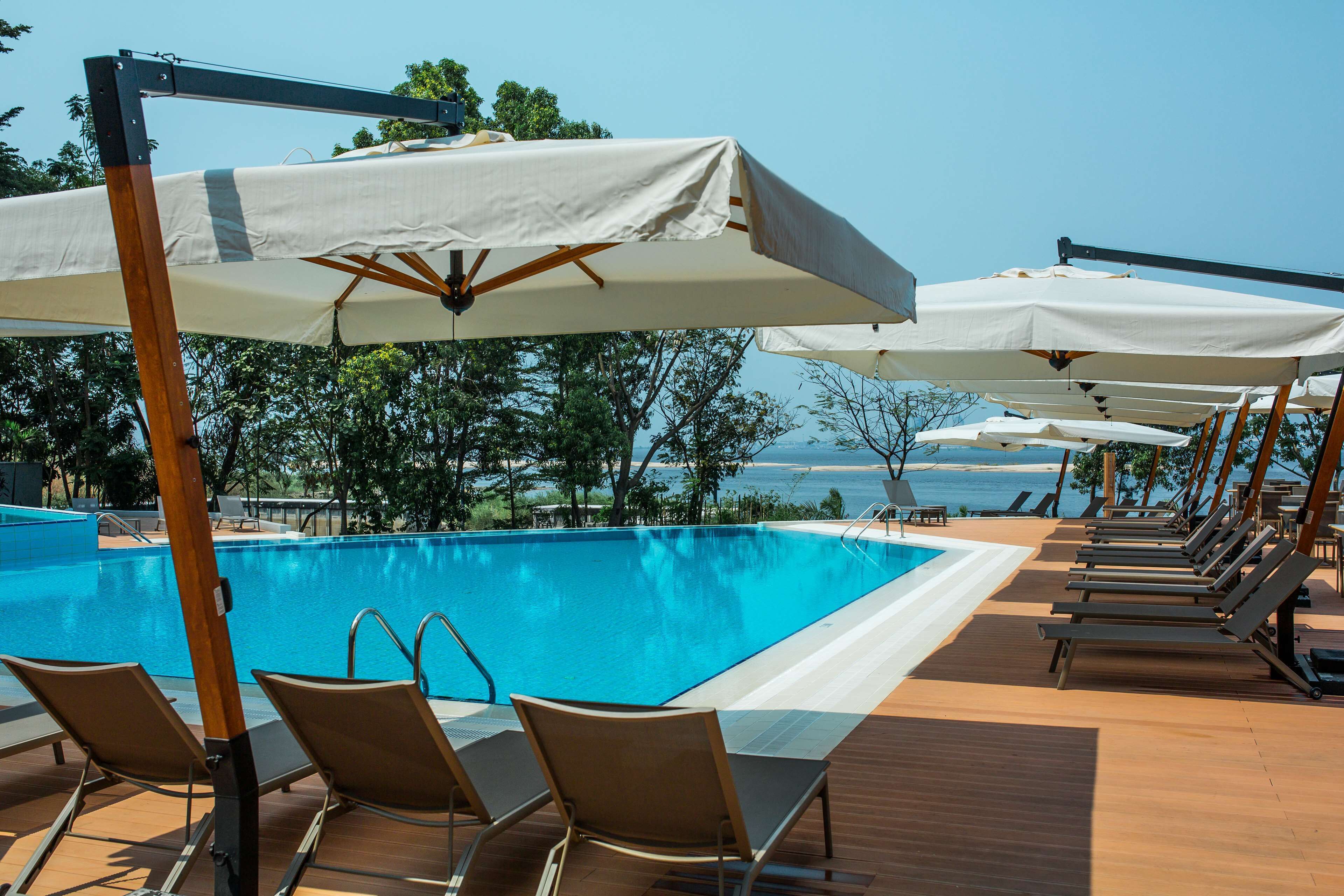 A poolside area with lounge chairs and umbrellas, overlooking a clear blue pool and the sea.