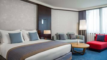 Une chambre d’hôtel avec un grand lit, un canapé, un fauteuil rouge, une petite table et une lampe.