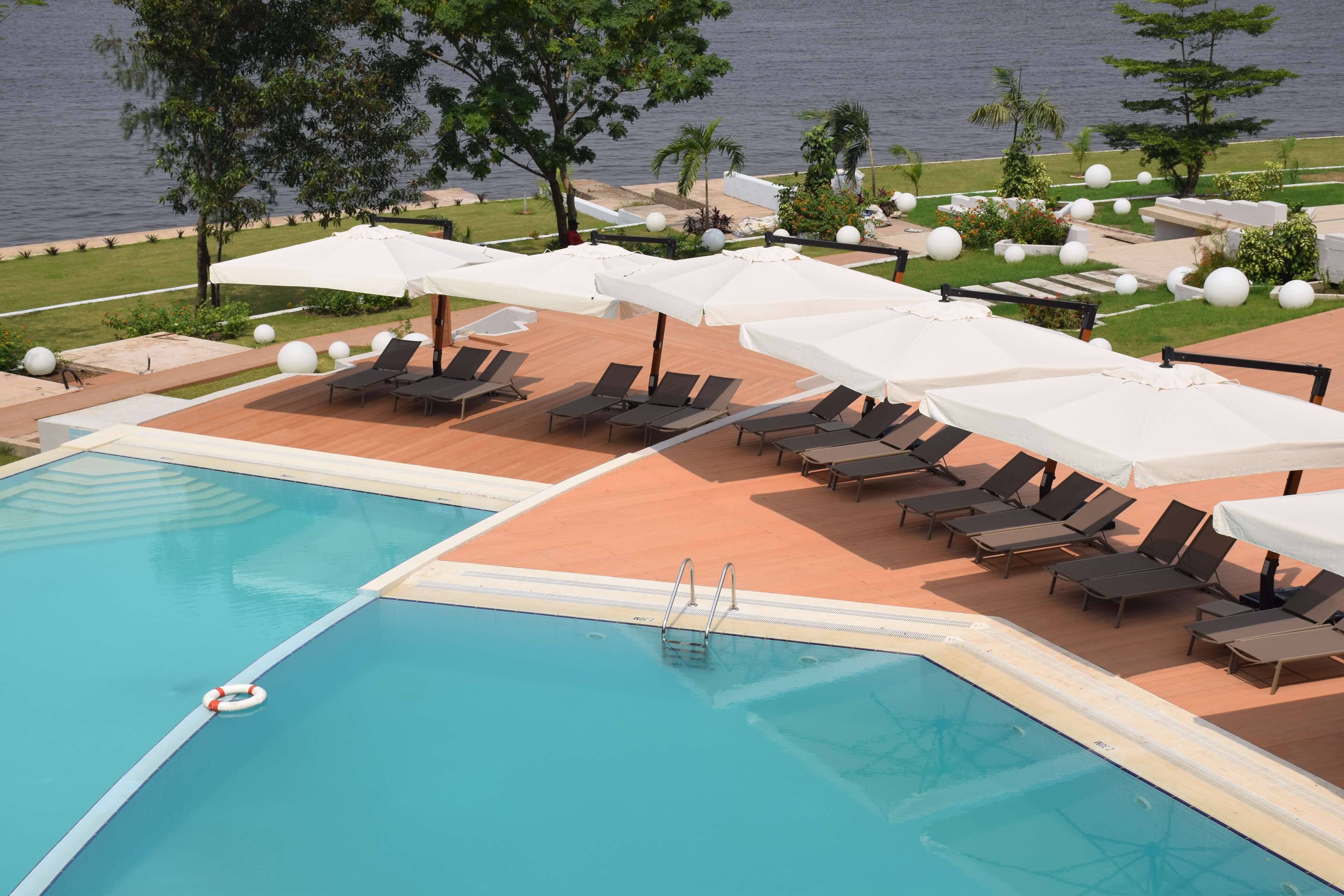 A pool area with lounge chairs and umbrellas, a lifebuoy, and a view of the water.