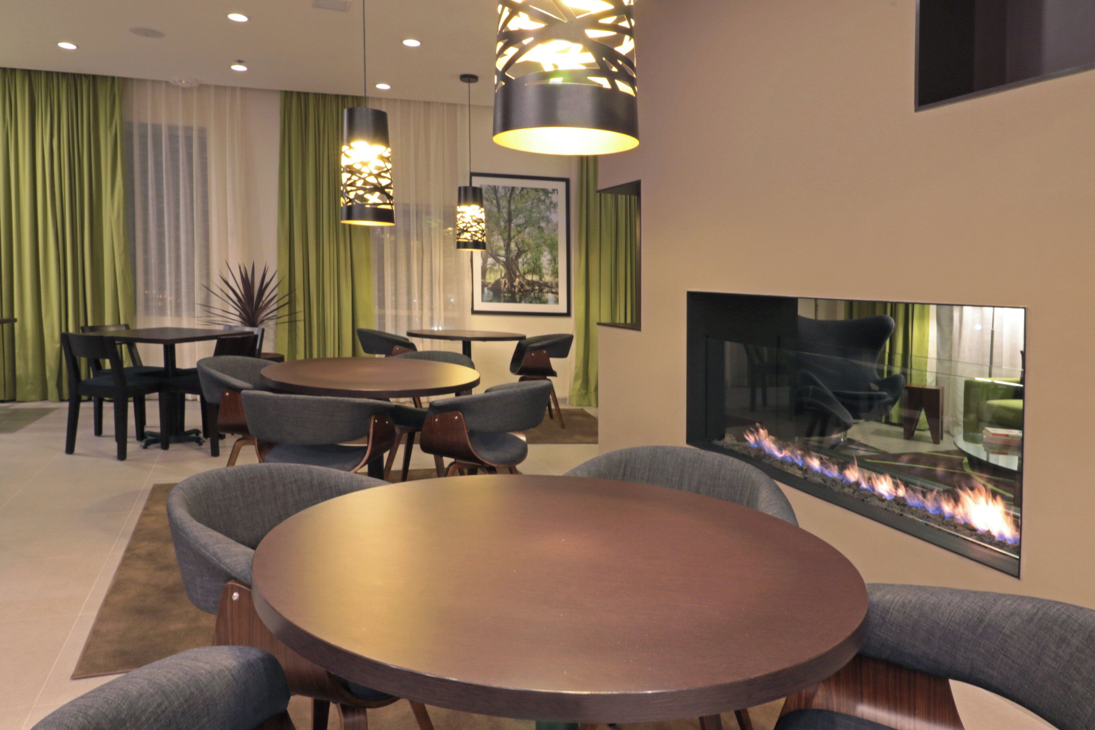 Un comedor moderno con mesas y sillas redondas, chimenea e iluminación decorativa.