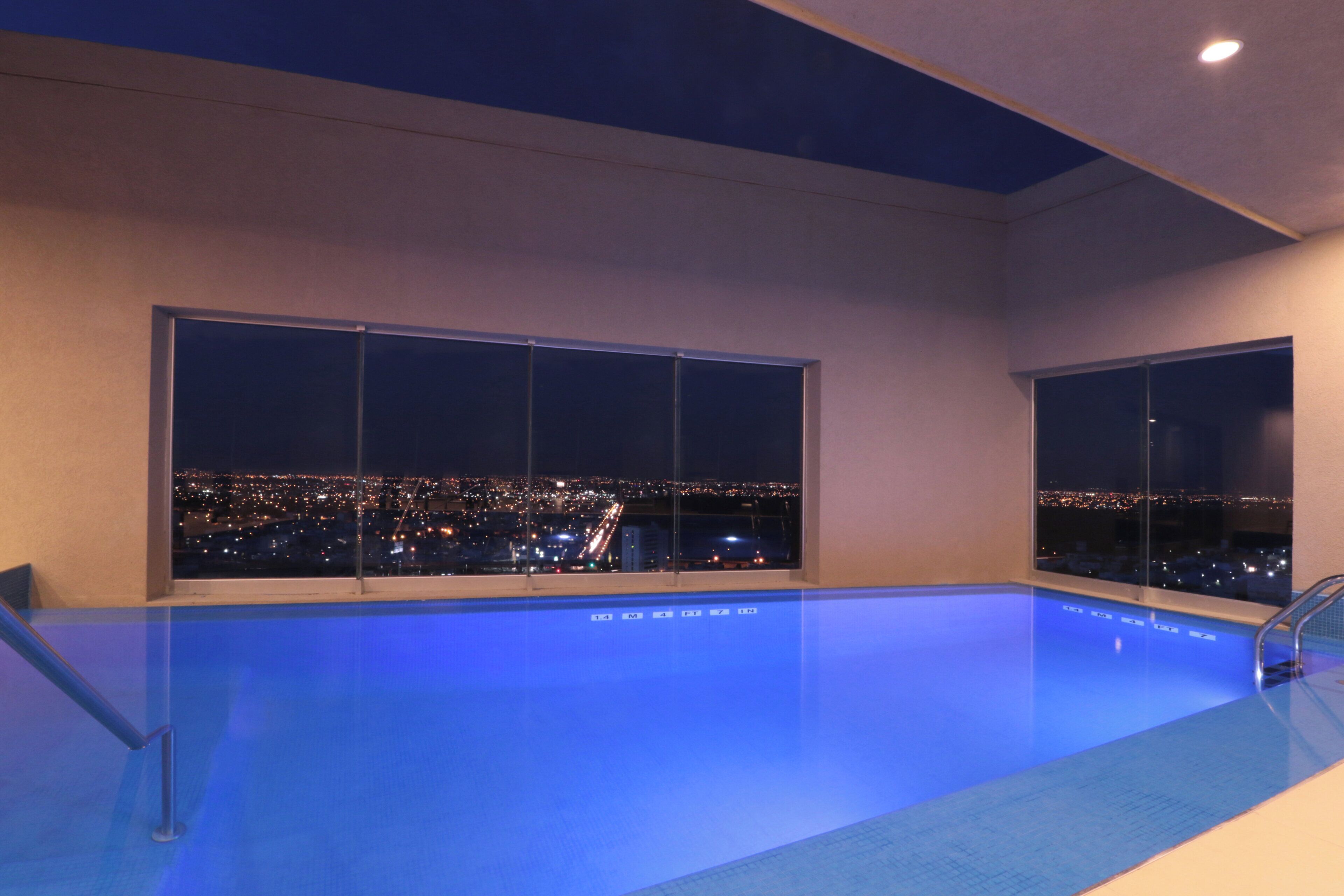 Una piscina interior moderna con grandes ventanales que ofrecen vistas a la ciudad de noche.