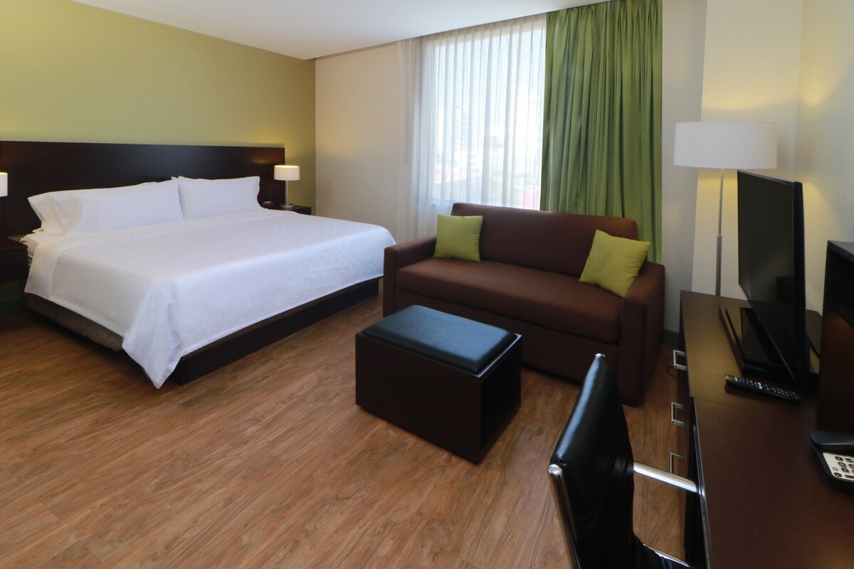 Habitación de hotel con una cama grande, un sofá, una mesita de centro y una televisión.