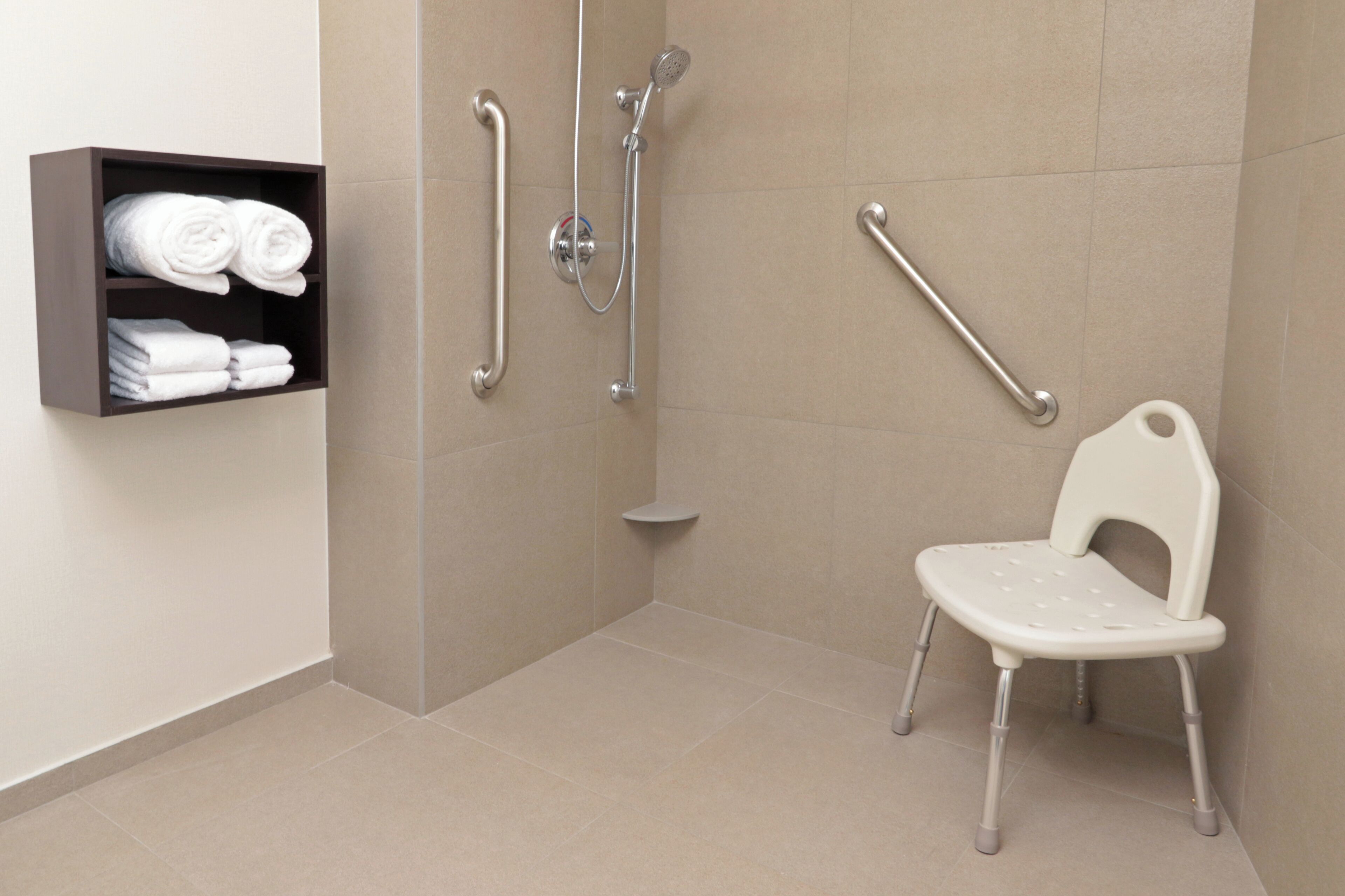 Une salle de bain équipée d’une douche, de barres d’appui, d’une chaise blanche et d’une étagère avec des serviettes.