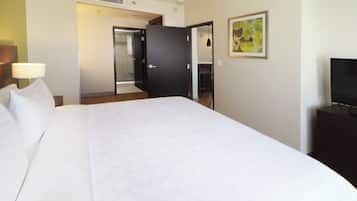 Una habitación de hotel con cama, televisor sobre un mueble, puerta que da a un baño y un cuadro en la pared.