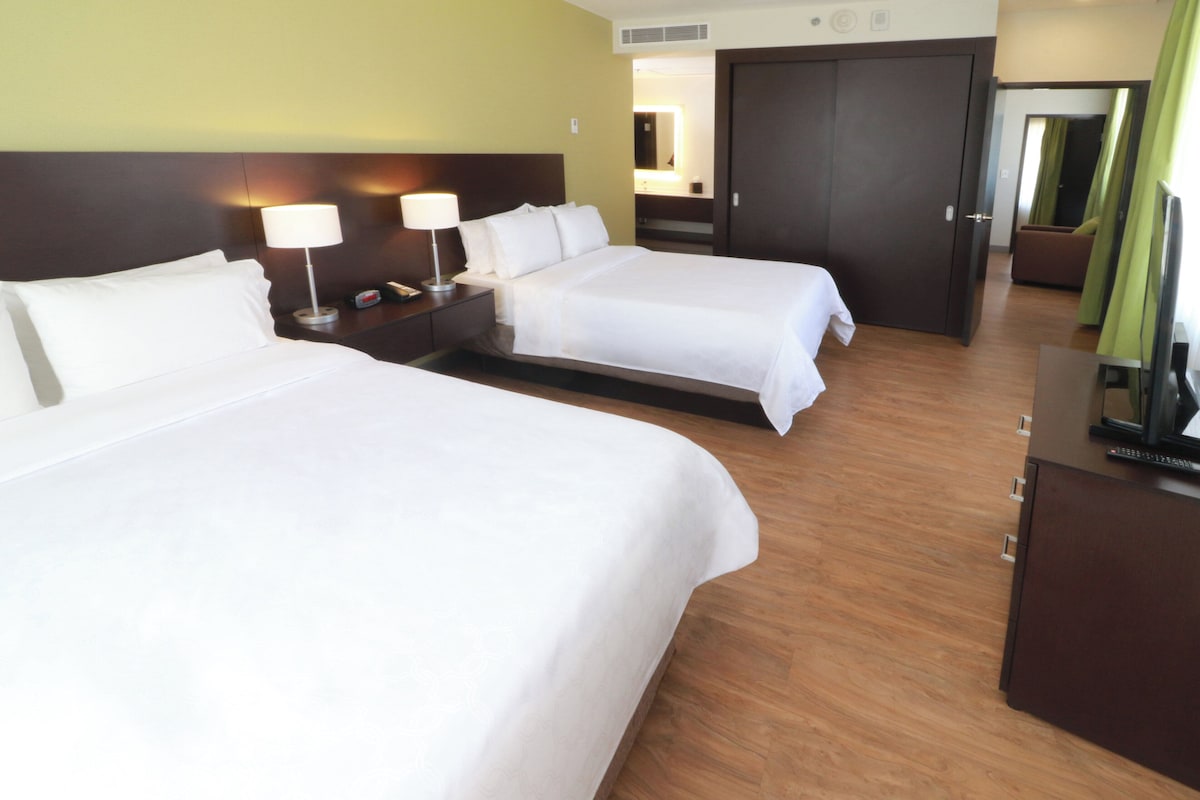 A hotel room with two beds, a nightstand with lamps, a mirror, and a TV.