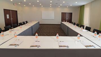Un salón de conferencias con una larga mesa, sillas, botellas de agua y una pantalla de proyector.