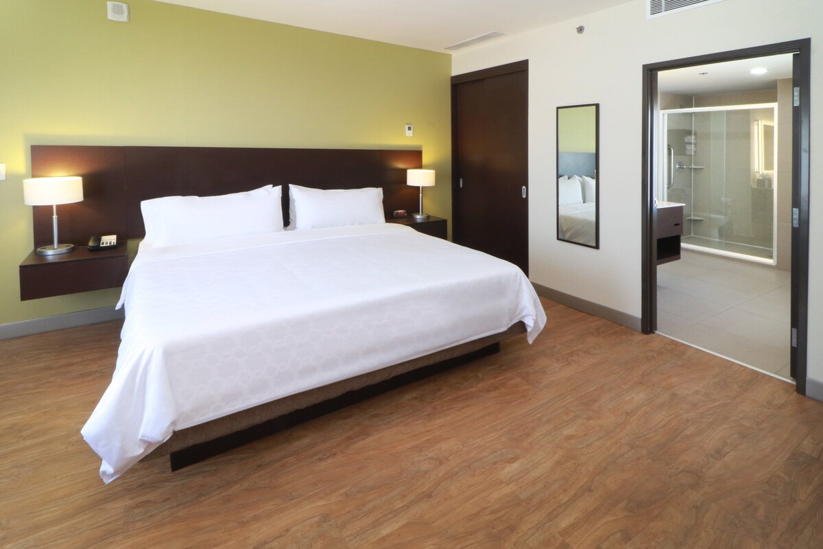 Habitación de hotel con una cama grande, lámparas de noche, un espejo y un vestidor.