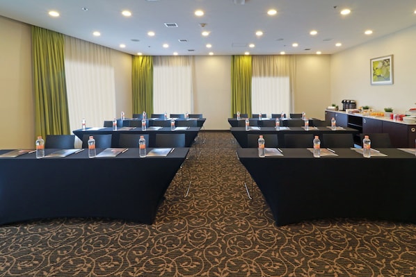Un salón de conferencias con una larga mesa, sillas, botellas de agua y una estación de café.