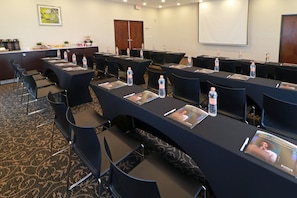 Un salón de conferencias con mesas, sillas, botellas de agua y folletos informativos.