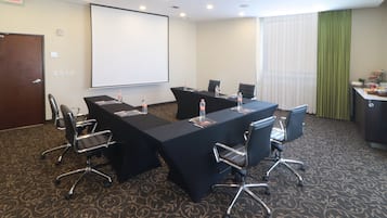 Un salón de conferencias con una larga mesa, sillas, una pantalla de proyector y un dispensador de agua.