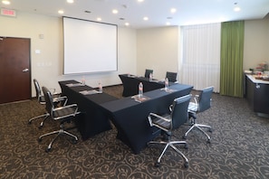 Un salón de conferencias con una larga mesa, sillas, una pantalla de proyector y un dispensador de agua.