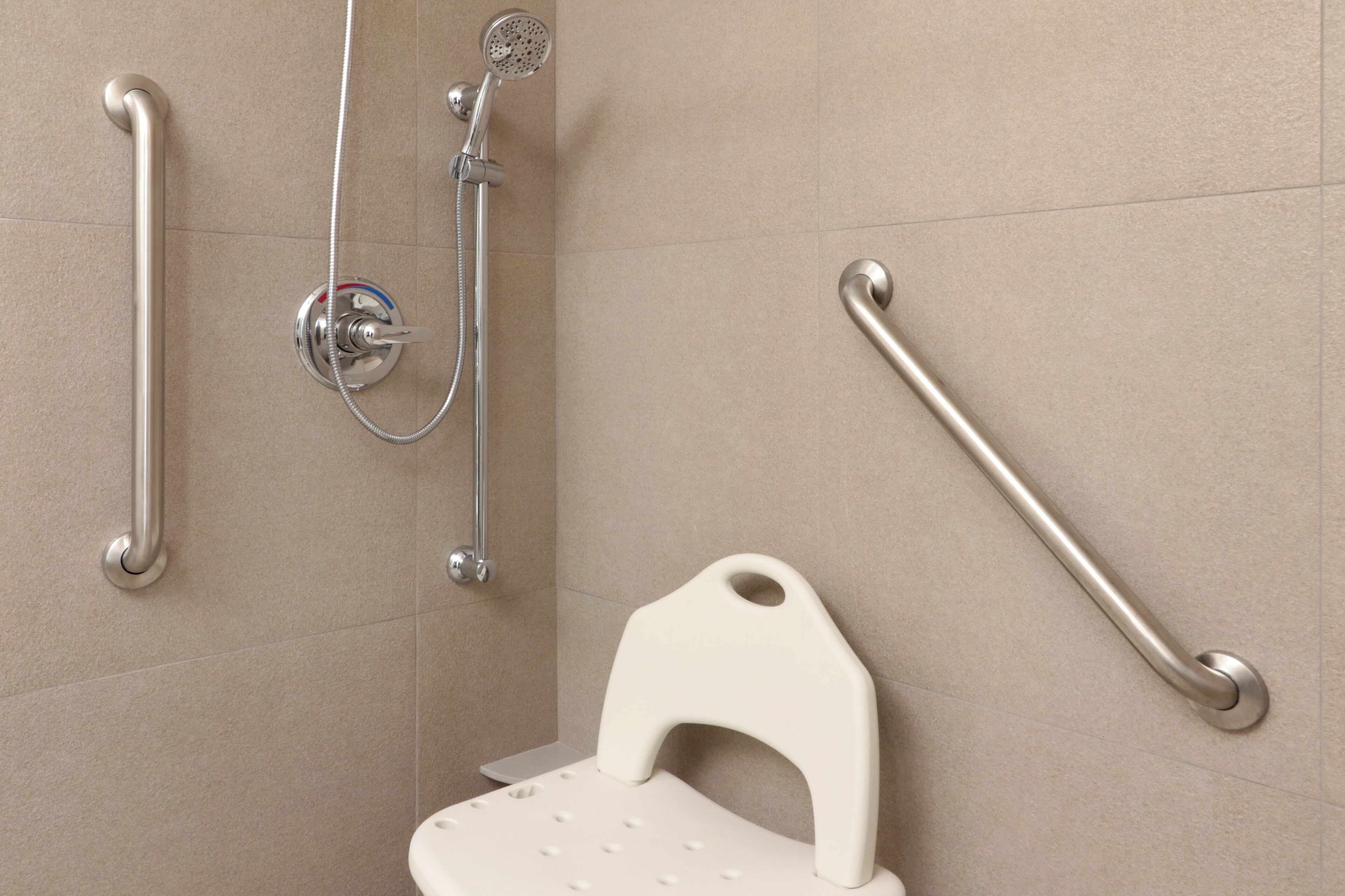 Ein Badezimmer mit Dusche, Haltegriffen und einem weißen Toilettensitz.
