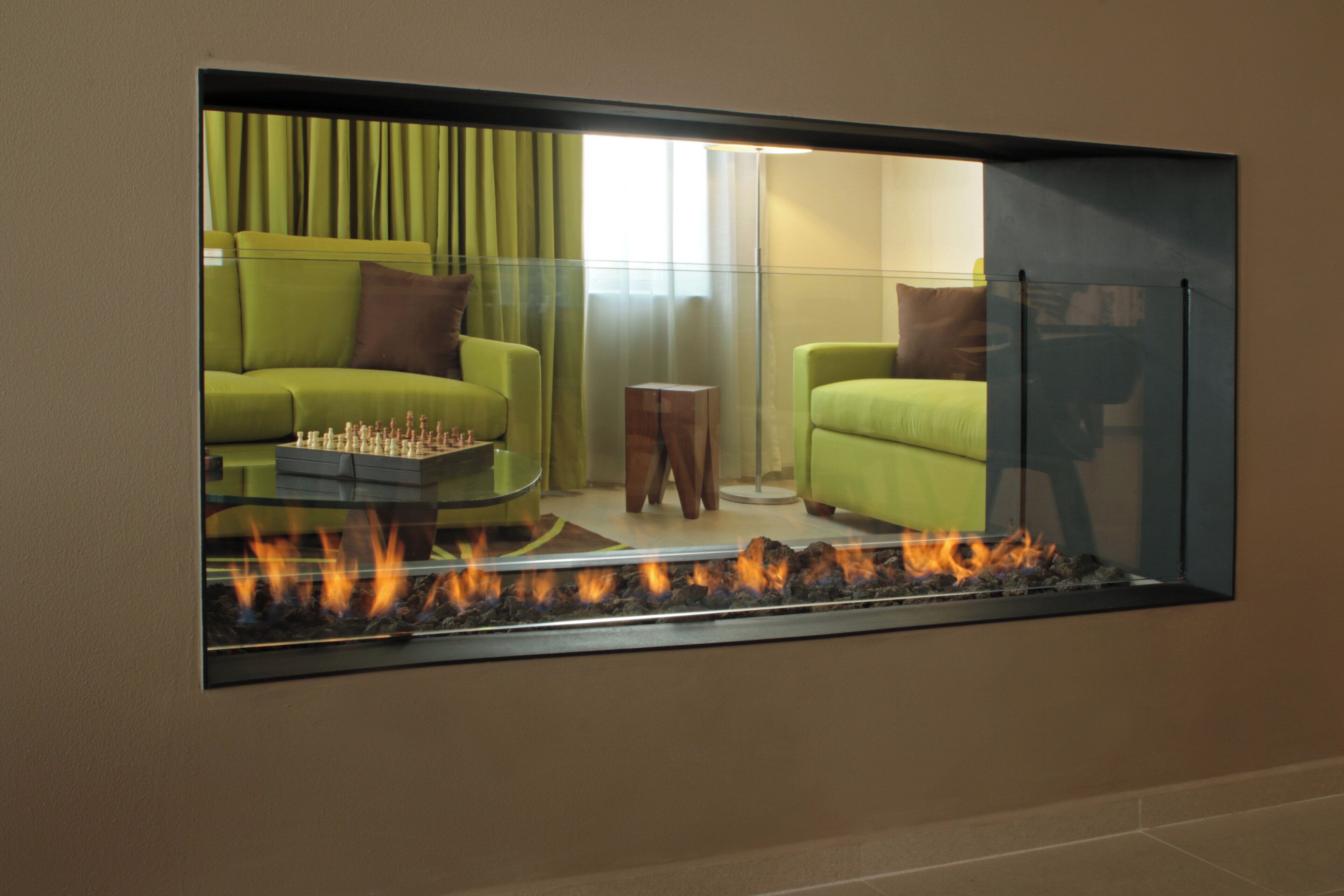 A living room with a glass fireplace, green sofas, and a chessboard.