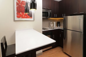 Una cocina moderna con armarios de madera oscura, un refrigerador de acero inoxidable, un microondas y una encimera blanca.