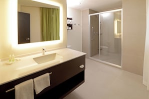Un baño moderno con un espejo grande, un lavamanos, una ducha y un inodoro.