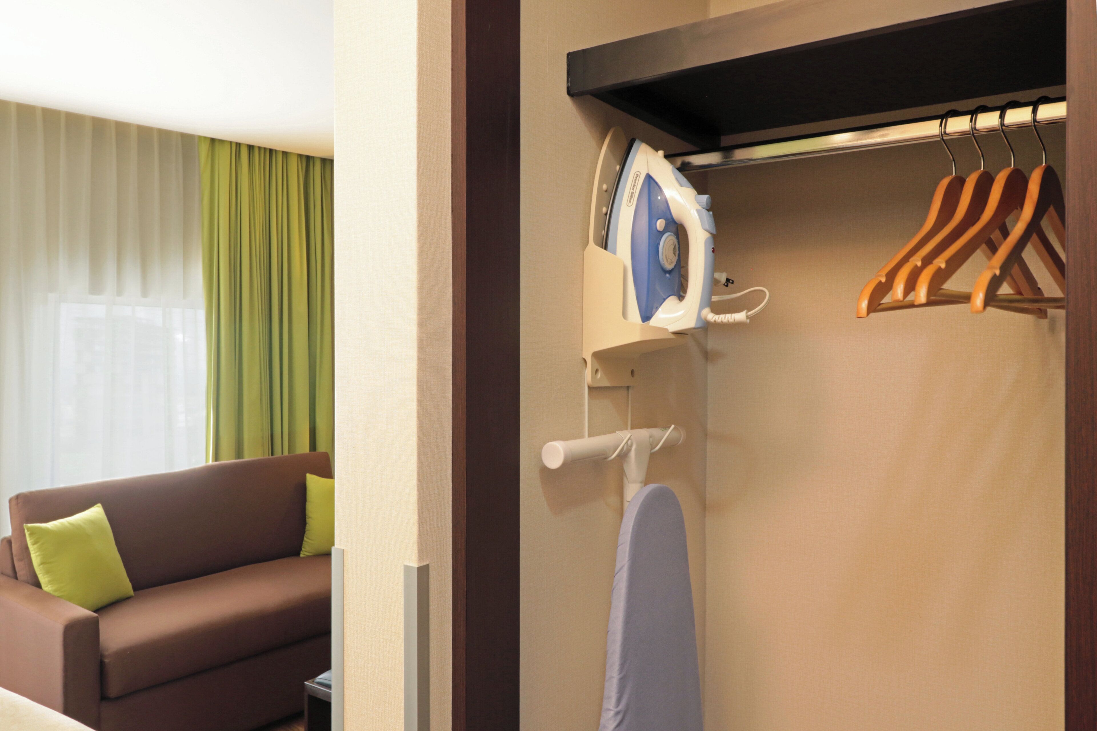 Ein Hotelzimmer mit einem braunen Sofa, einem hängenden Bügeleisen und einem Kleiderständer mit Kleiderbügeln.