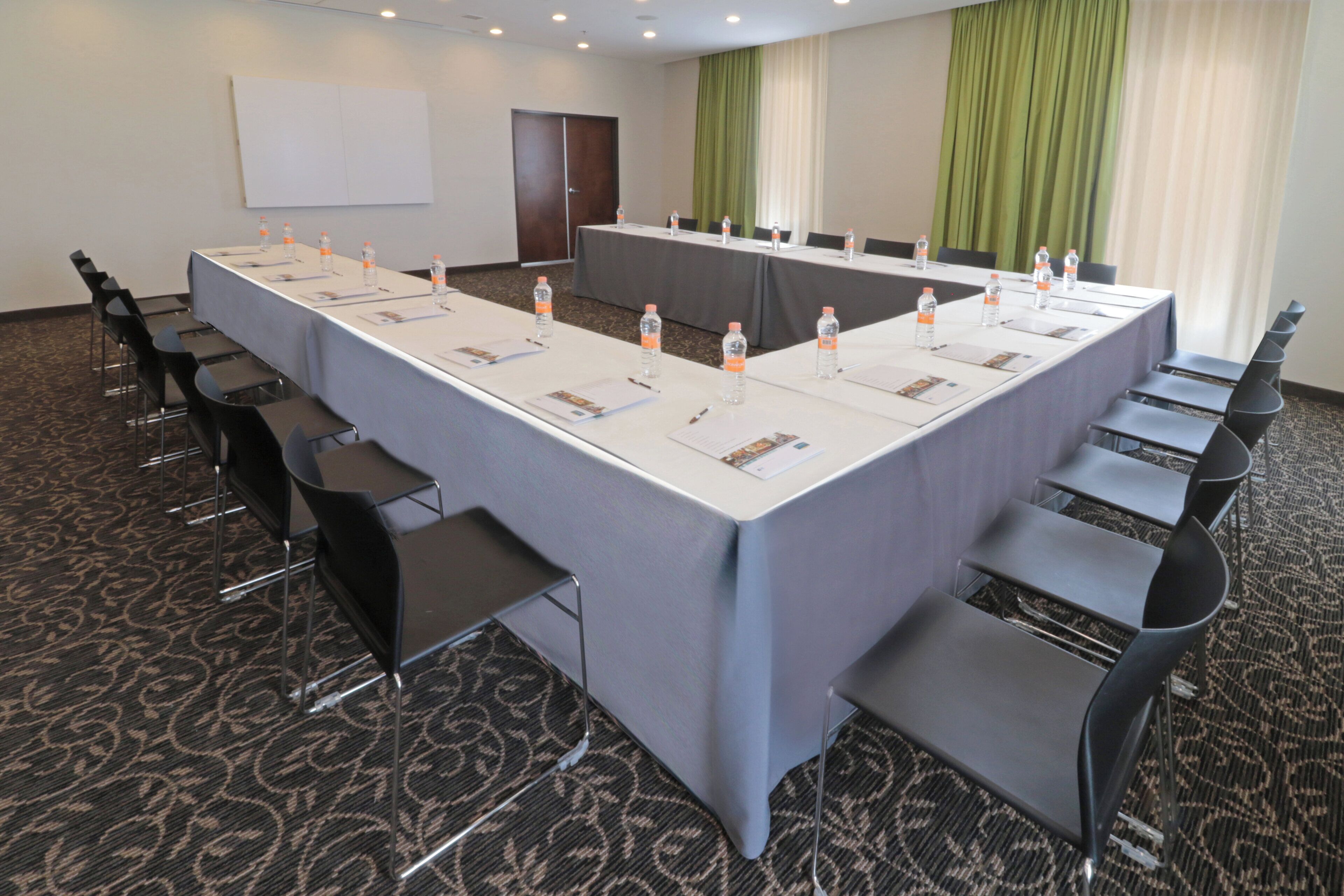 A conference room with a long table, chairs, water bottles, and a projector screen.