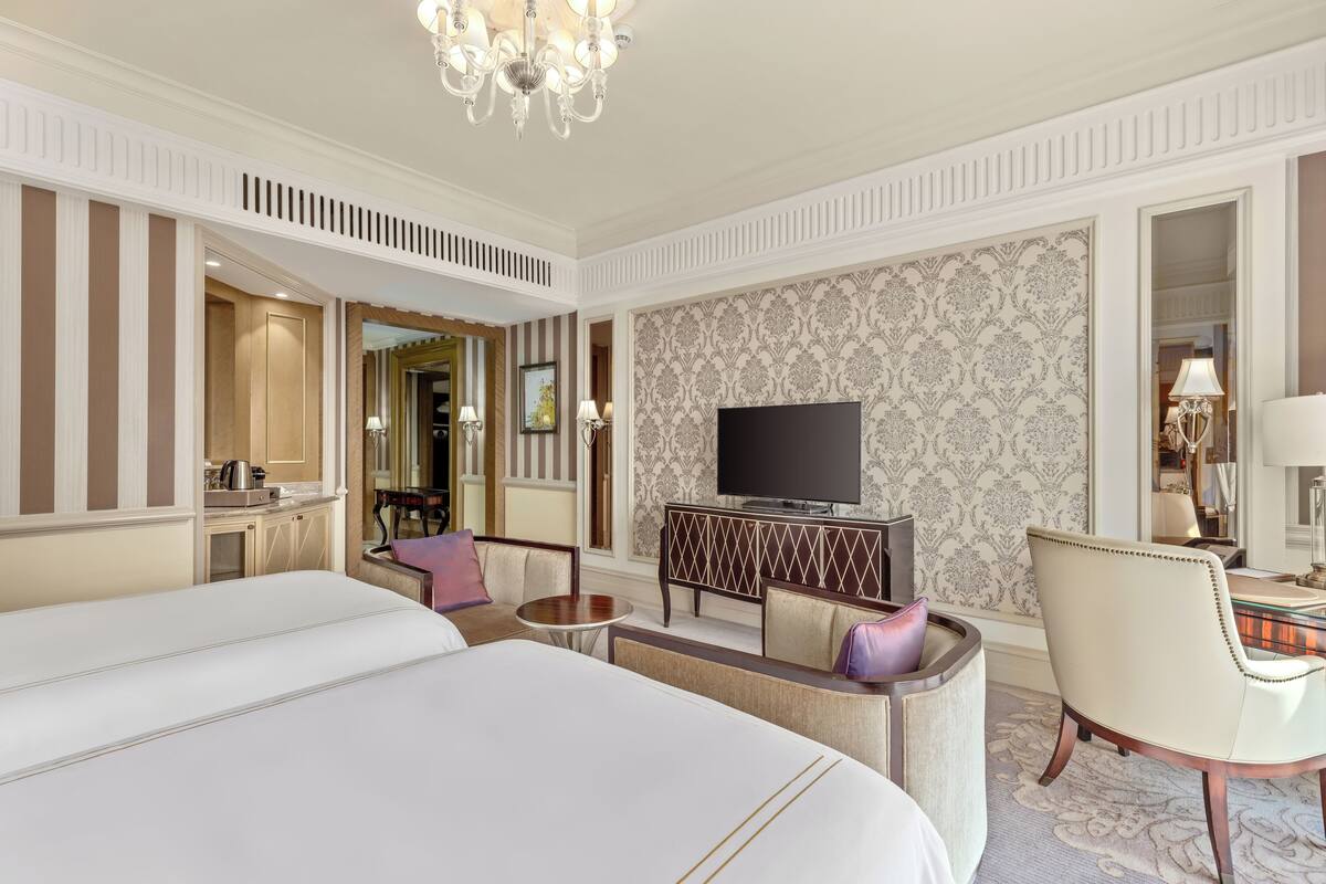 A hotel room with a large bed, a TV, a seating area with a table and chairs, and a decorative mirror.
