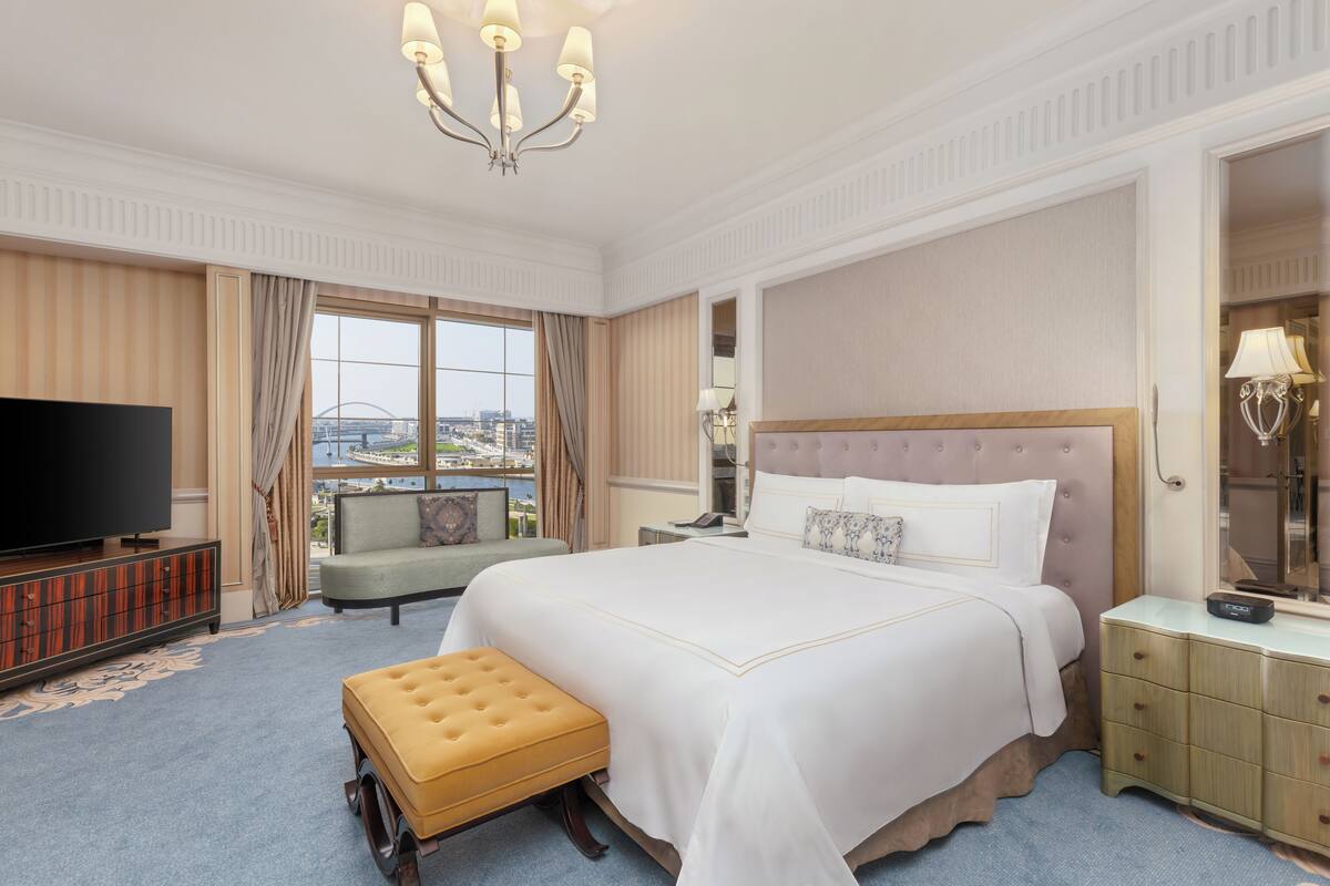 A hotel room with a large bed, a television, a sofa, and a view of the city.