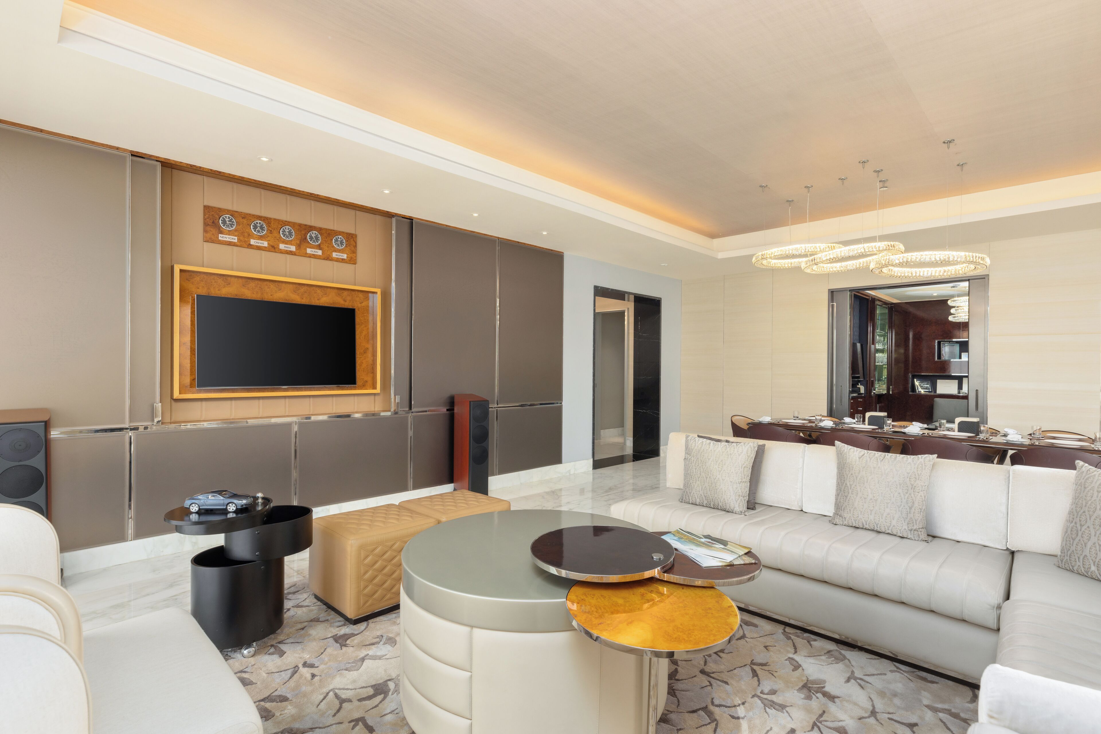 A modern living room with a large flat-screen TV, a sofa, a coffee table, and a dining area with a chandelier.