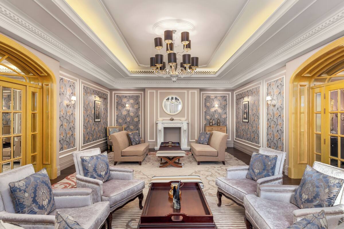 A luxurious living room with ornate wallpaper, a grand chandelier, and classic furniture.