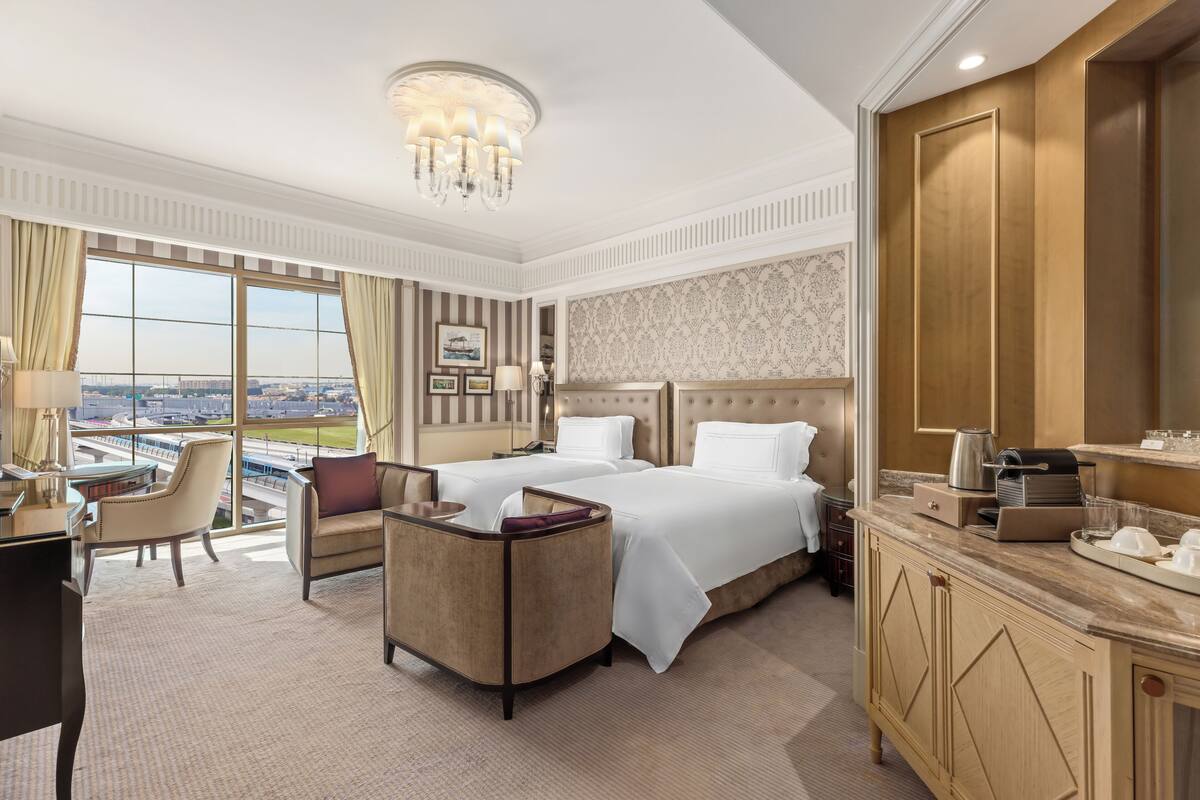 A hotel room with a large bed, two bedside tables, a desk, a chair, and a view of a cityscape.