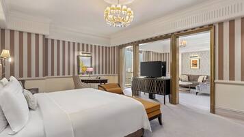 Une chambre d’hôtel avec un grand lit, un bureau avec une lampe, une télévision et une vue sur l’espace de vie, grâce à une porte ouverte.