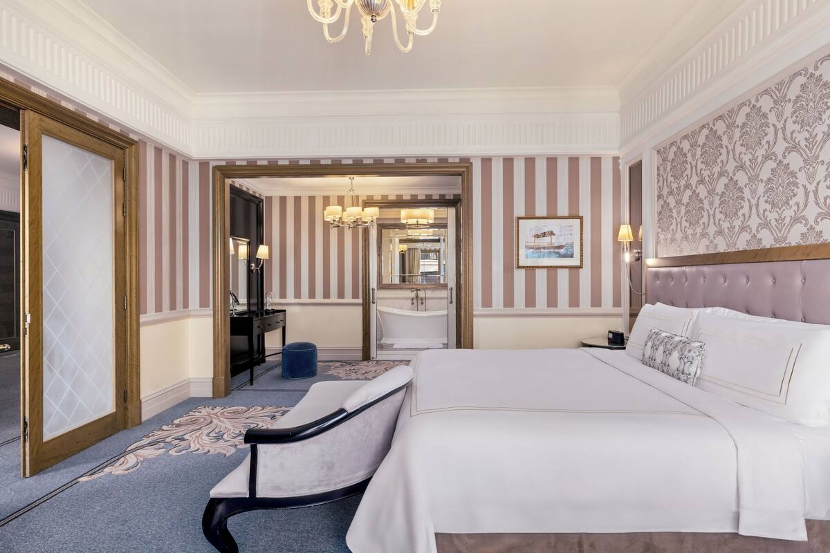 A spacious hotel room with a large bed, a sitting area, a bathroom, and a view of the hallway.