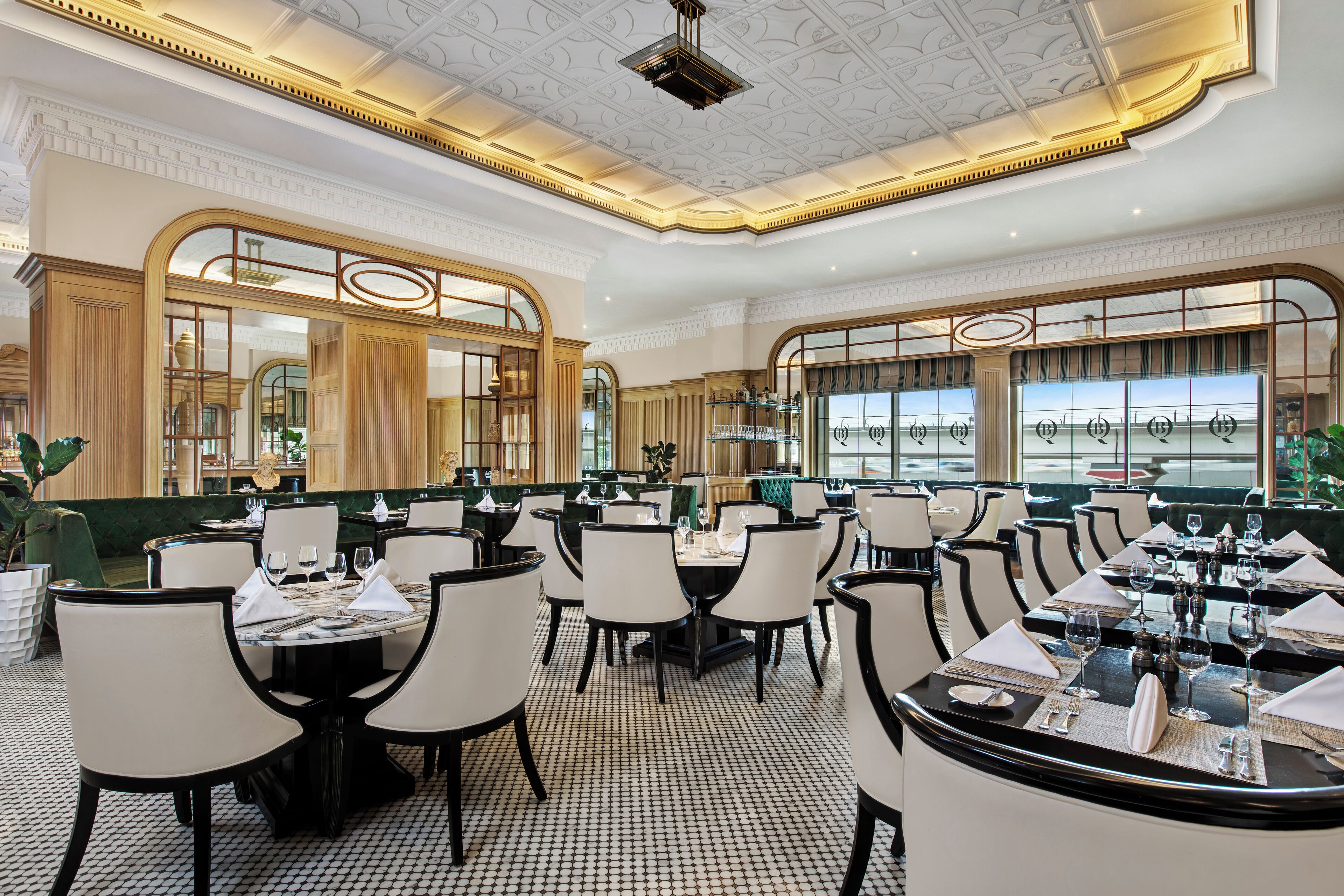 A spacious restaurant with multiple dining tables and chairs, large windows with a view, and a decorative ceiling.