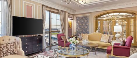 A luxurious living room with a large flat-screen TV, plush seating, a chandelier, and a view of the city.