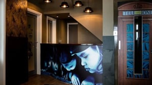 A reception area with a large screen displaying a movie scene, a telephone booth, and pendant lighting. - An Mor Hotel (Bude)