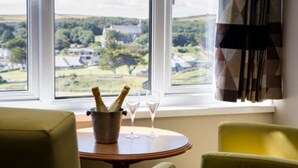 A room with a view of a rural landscape, a table with a bucket of champagne and glasses, and a green armchair. - An Mor Hotel (Bude)