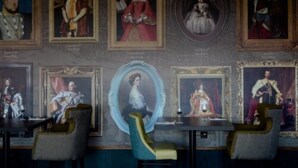 A room with a wall adorned with framed portraits, a round mirror, and a table with chairs. - An Mor Hotel (Bude)