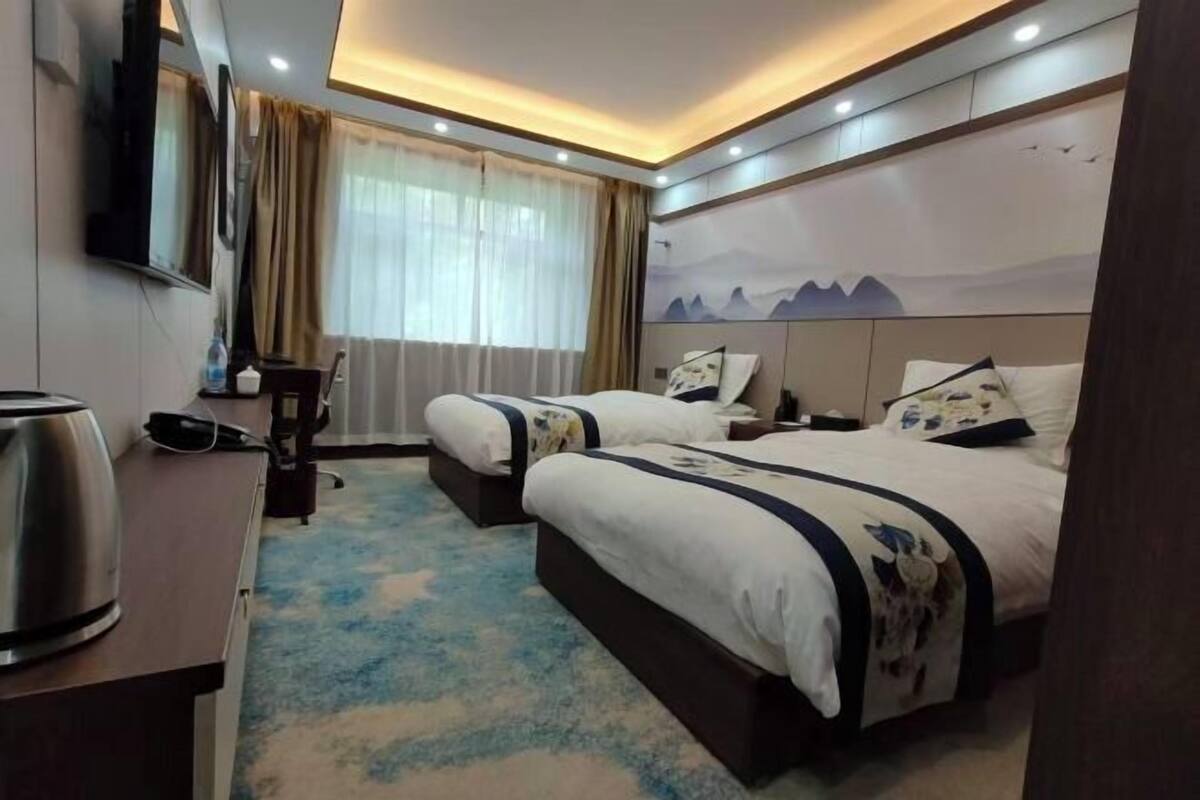 A hotel room with two beds, a desk, a television, and a window with curtains.