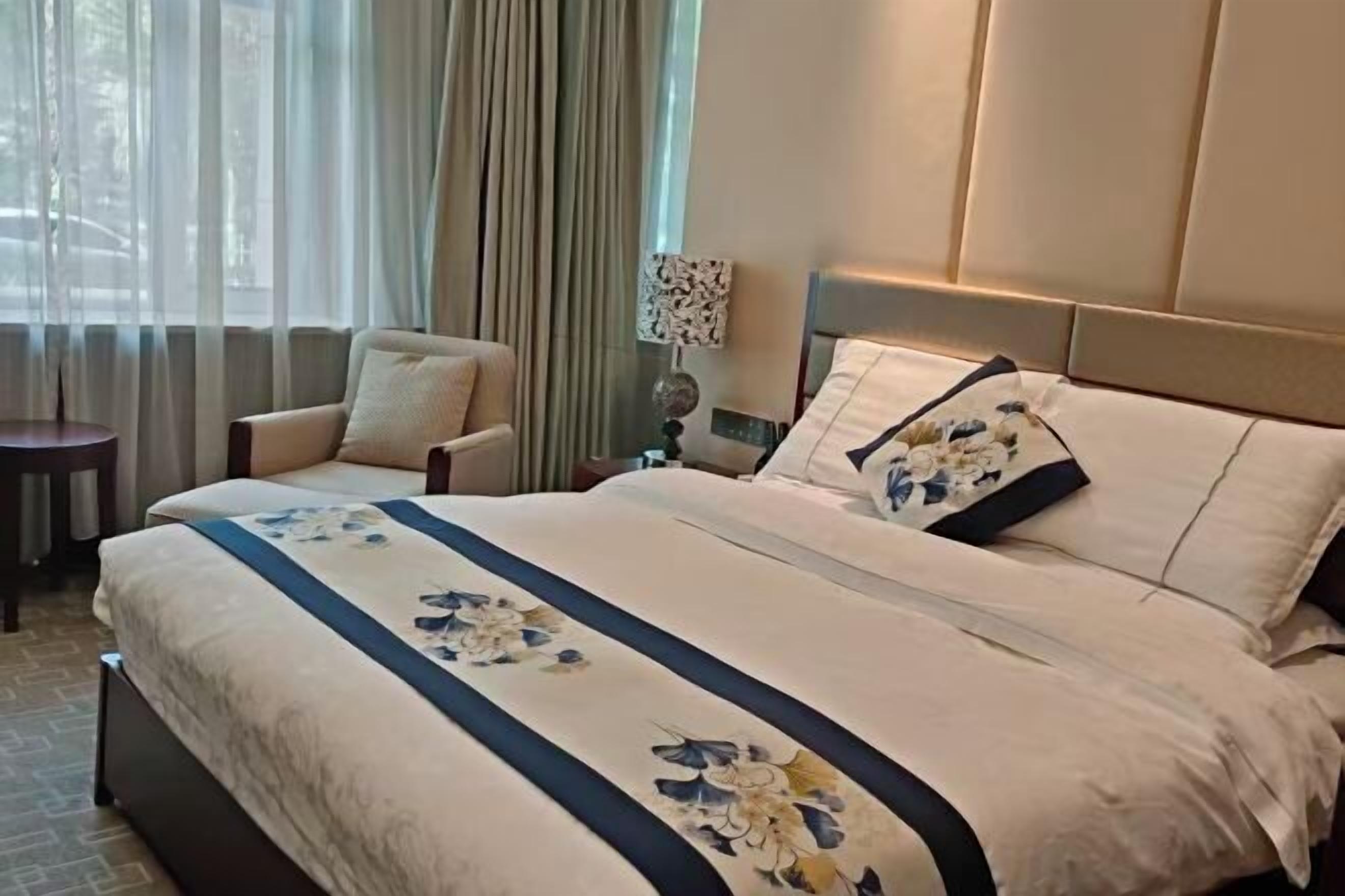 A hotel room with a large bed, a chair, a lamp, and a view of the outdoors.