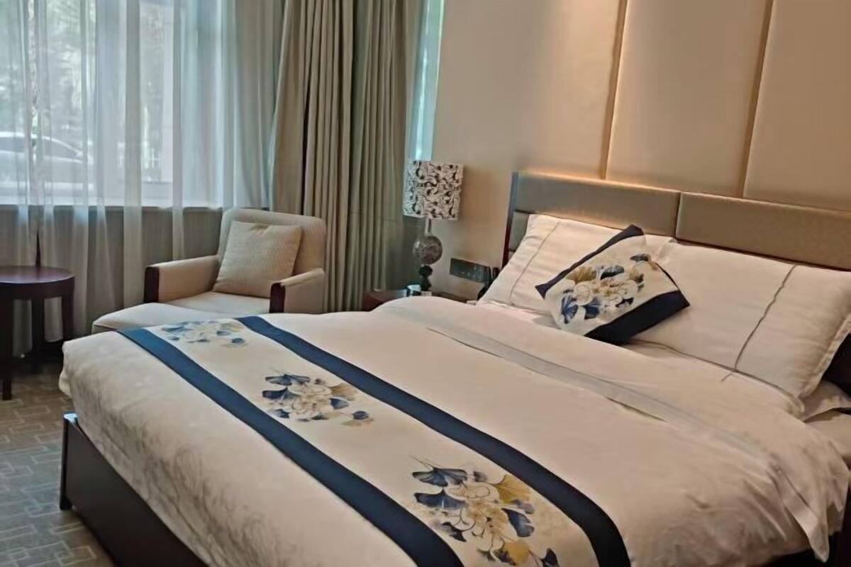 A hotel room with a large bed, a chair, a lamp, and a view of the outdoors.