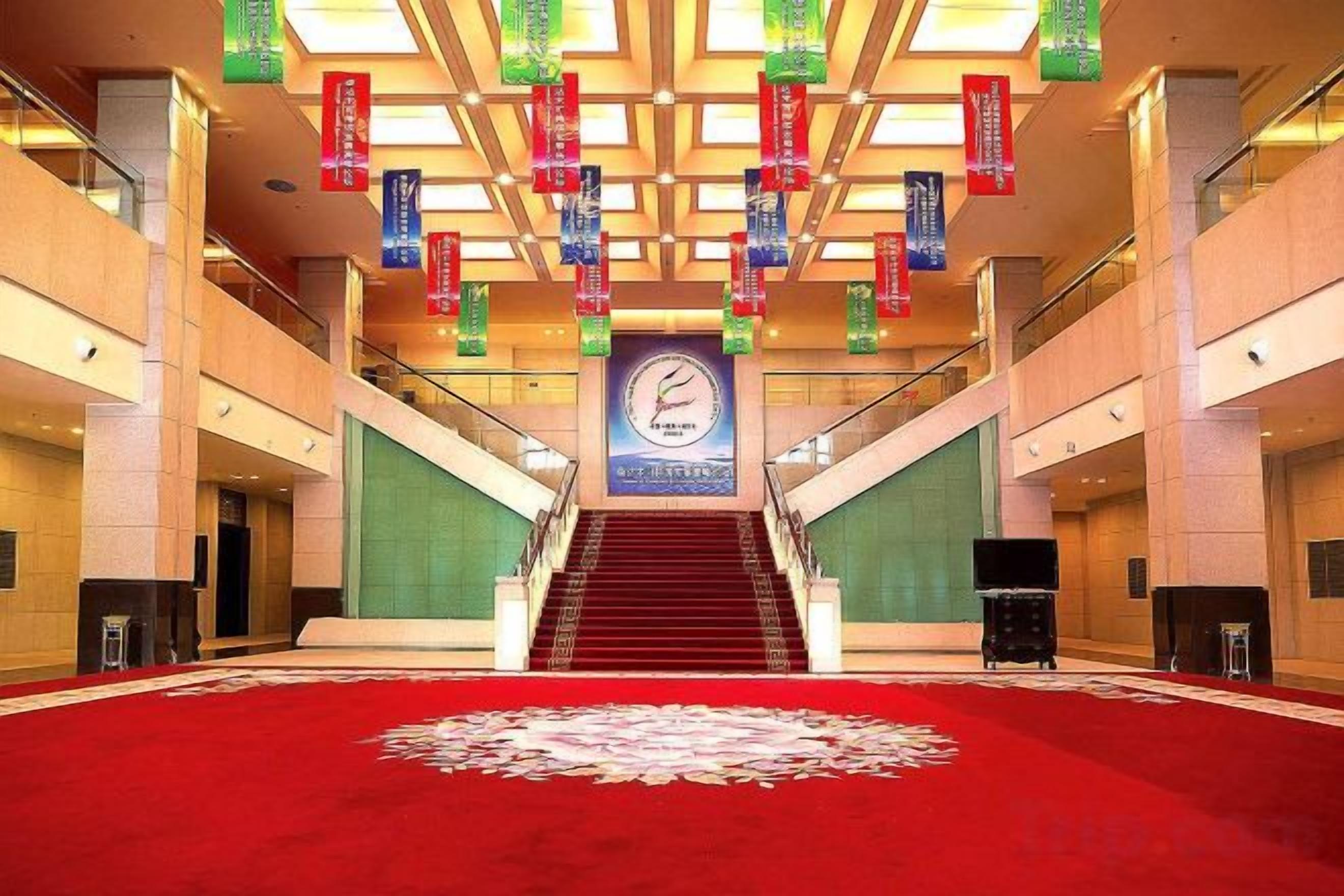 Eine Hotellobby mit rotem Teppich, einer Uhr und einer Treppe zu den oberen Etagen.