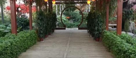 Un camí de fusta que serpenteja per un jardí amb una pèrgola i fanals.