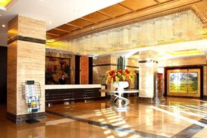 A hotel lobby with a reception desk, a large vase of flowers, and a painting on the wall. - Golmud Hotel (Golmud)