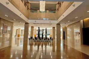 Un vestíbulo espacioso con techos altos, pisos pulidos y una columna central con plantas en macetas.