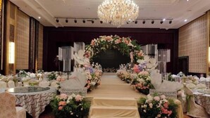 Un escenario con decoración floral, una araña y una disposición formal de asientos en un salón de banquetes.