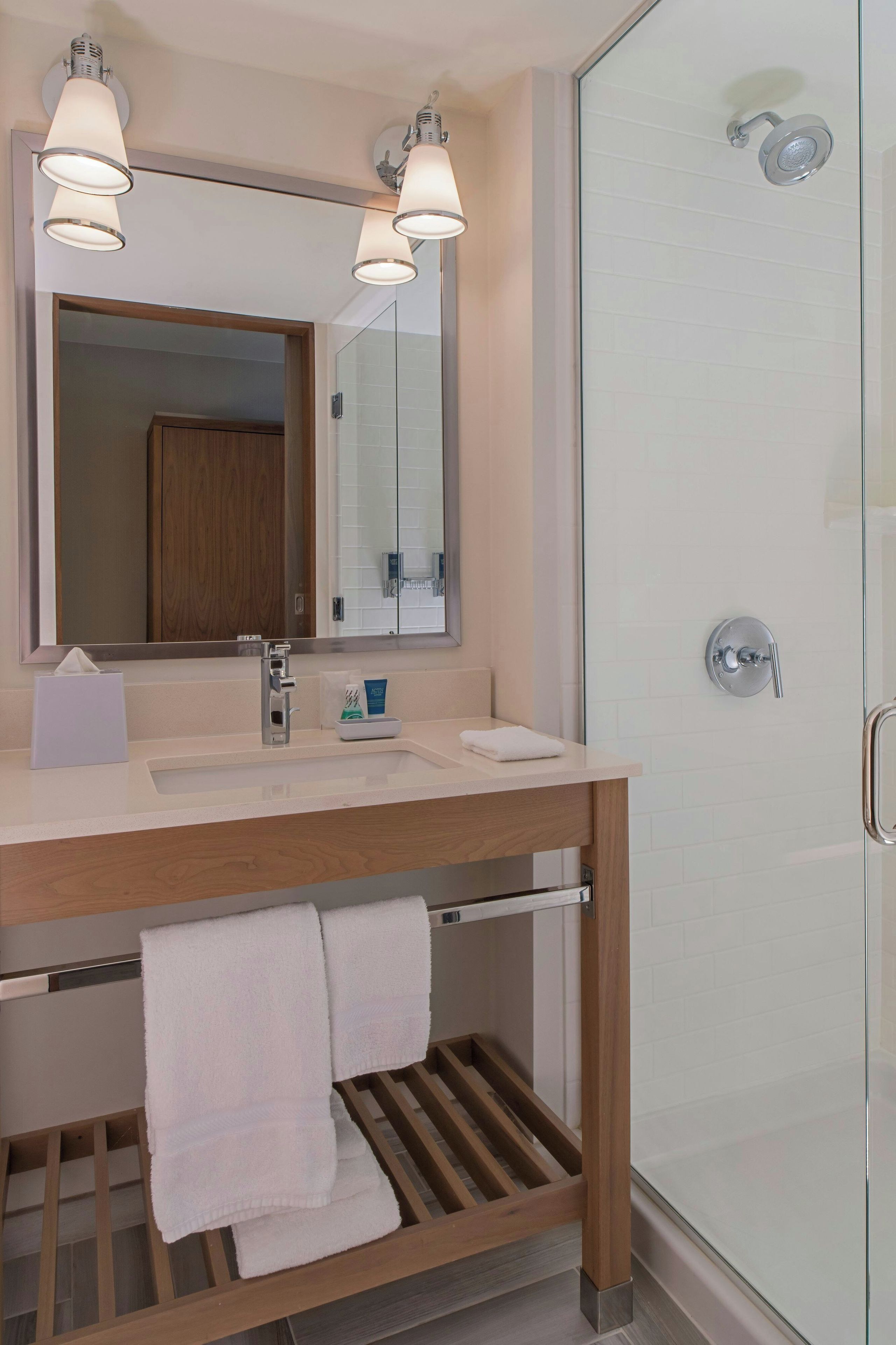 Un baño moderno con cabina de ducha de vidrio, tocador de madera con espejo y un perchero para toallas.