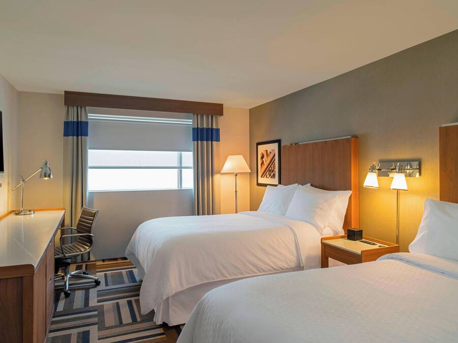 A hotel room with two beds, a desk, a chair, a TV, and a window with curtains.