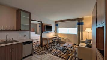 Habitación de hotel compacta con kitchenette, una cama, un escritorio con silla, un televisor y un sofá.