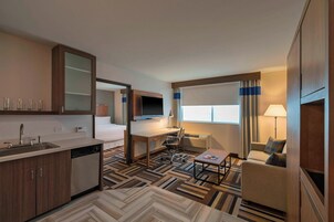 Habitación de hotel pequeña con kitchenette, una cama, un escritorio, una silla, un televisor y un sofá.