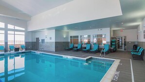 An indoor swimming pool with clear water, surrounded by lounge chairs and a tiled floor.