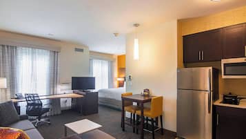Habitación de hotel con cama, escritorio, silla, pequeña mesa, sofá, kitchenette con refrigerador y microondas, y televisor.